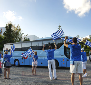 Menschen schwingen Griechenland-Flaggen vor TUI Reisebus.