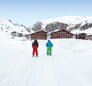 Zwei Personen, die in Richtung einer Skihütte fahren.